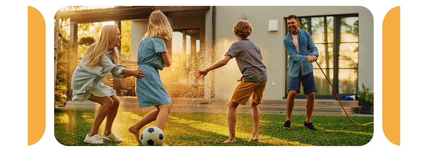 a man playfully spraying his family with a water hose as they laugh and scramble